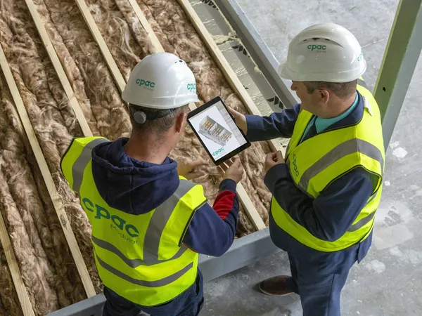 Técnicos com capacete avaliando uma obra com tablet