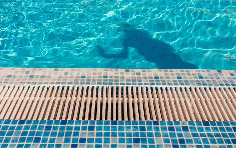 Borda de piscina com pastilhas azuis e grelha de transbordo