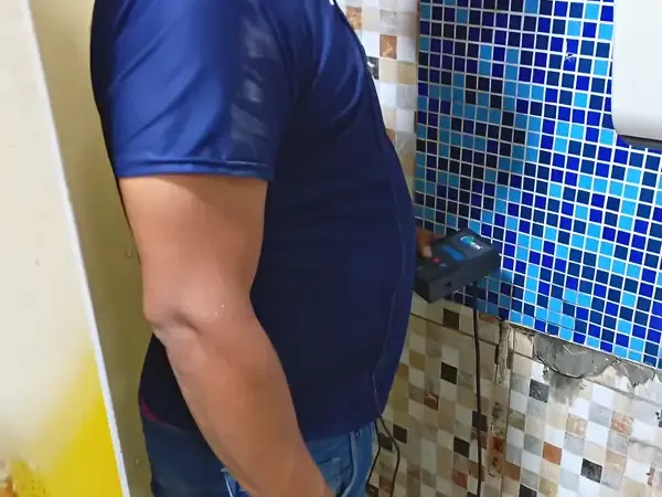 Técnico da Hidequel com geofone encostado na parede do banheiro